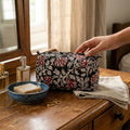 Person opening a floral-patterned makeup bag on a wooden surface with various items around.