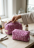 Person holding a pink toiletry bag on a bathroom counter with various items.